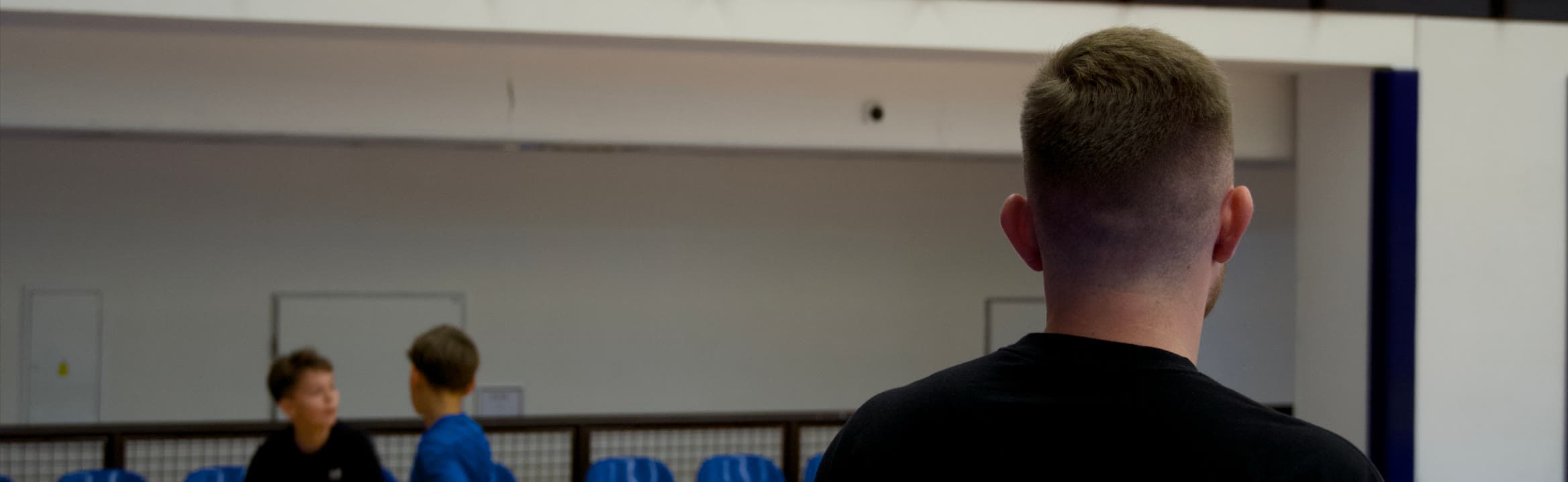 Ondra zezadu sleduje dva mladé hráče při tréninku v hale