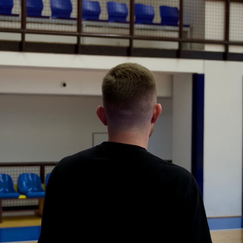 Ondra zezadu sleduje dva mladé hráče při tréninku v hale
